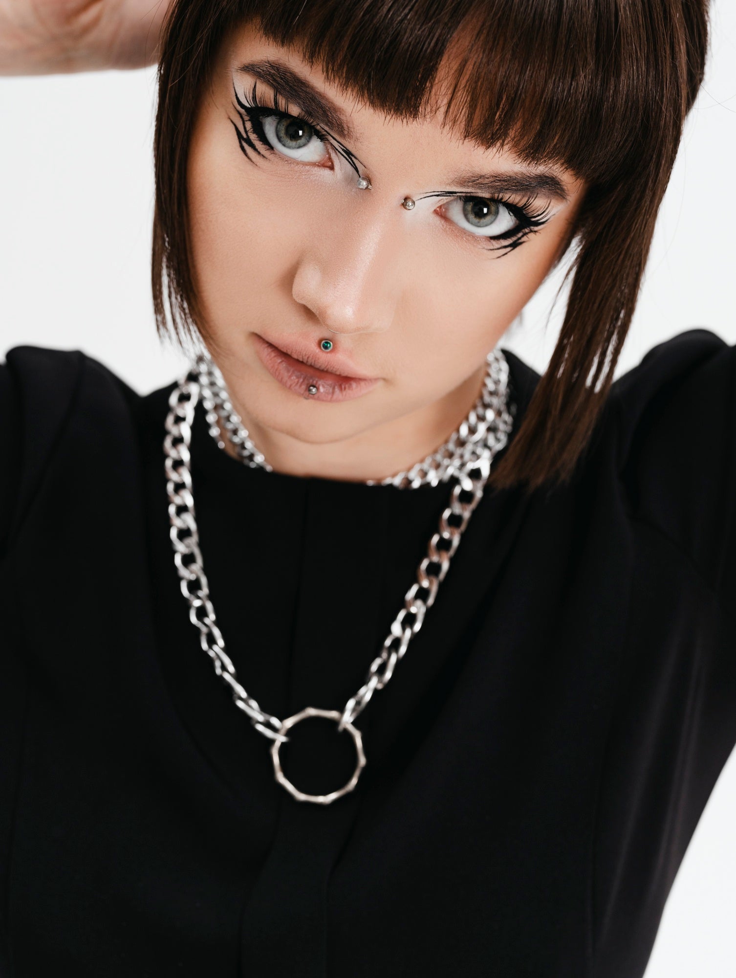 Person wearing a black outfit with a silver chain necklace on a white background