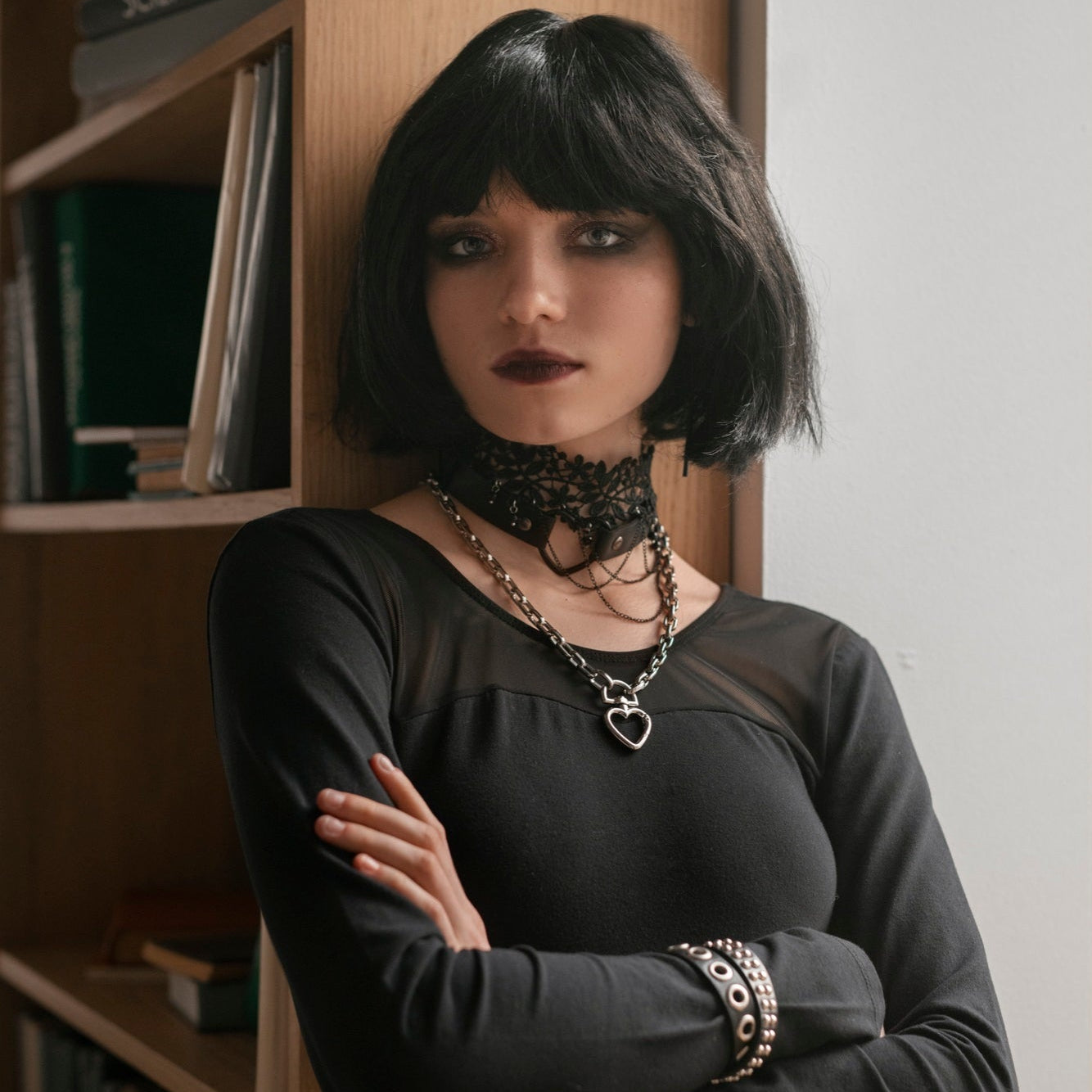 Woman in a black outfit with jewelry standing in a room with a bookshelf.