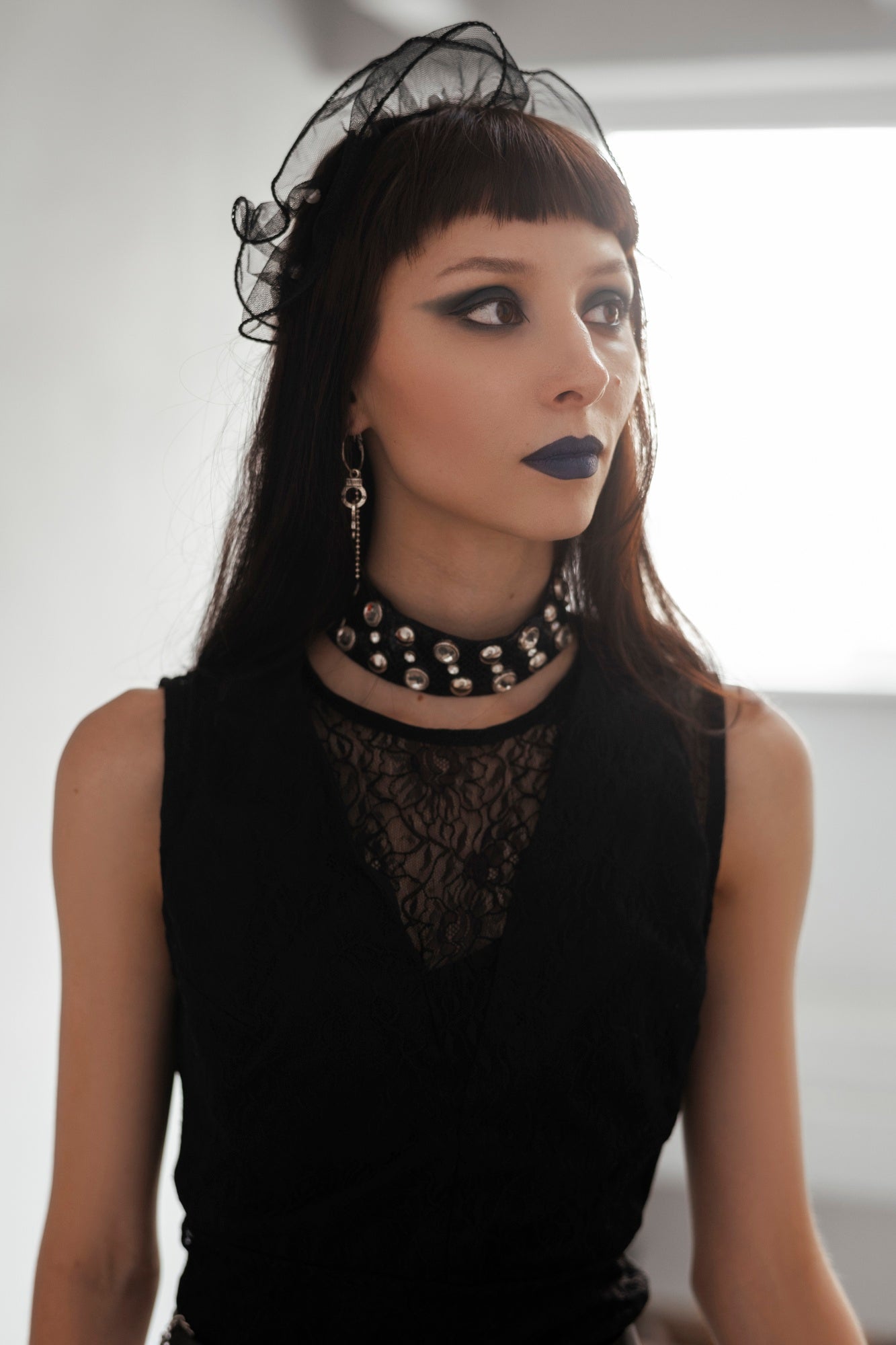 Woman wearing a black lace dress with a sheer headband and dark lipstick.