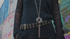 Close-up of gothic mesh top with layered silver pendant necklace and studded belt, showcasing modern dark fashion details.